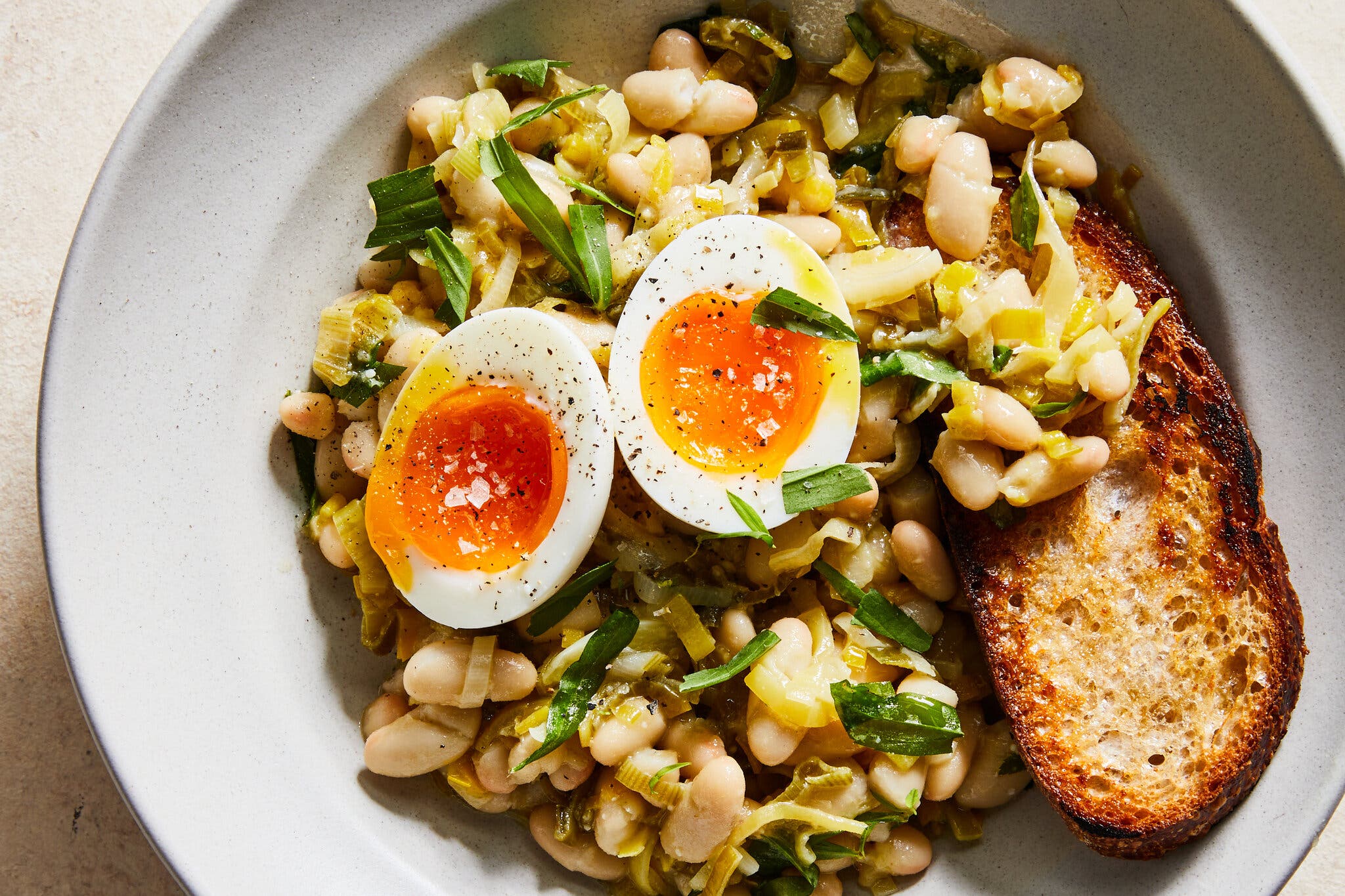 White beans and strips of leeks sit nestled in a bowl and topped with jammy eggs.