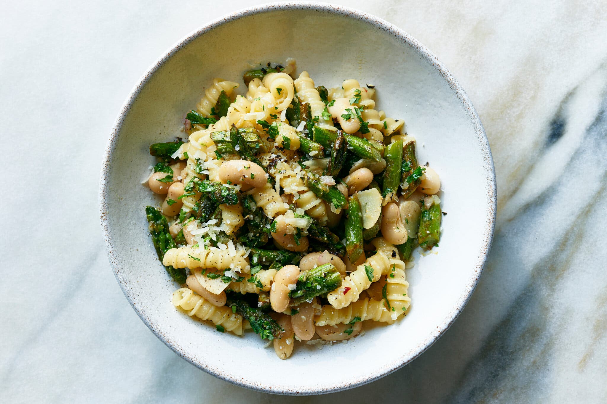 Short curly pasta is tossed with white beans and asparagus in a white bowl.