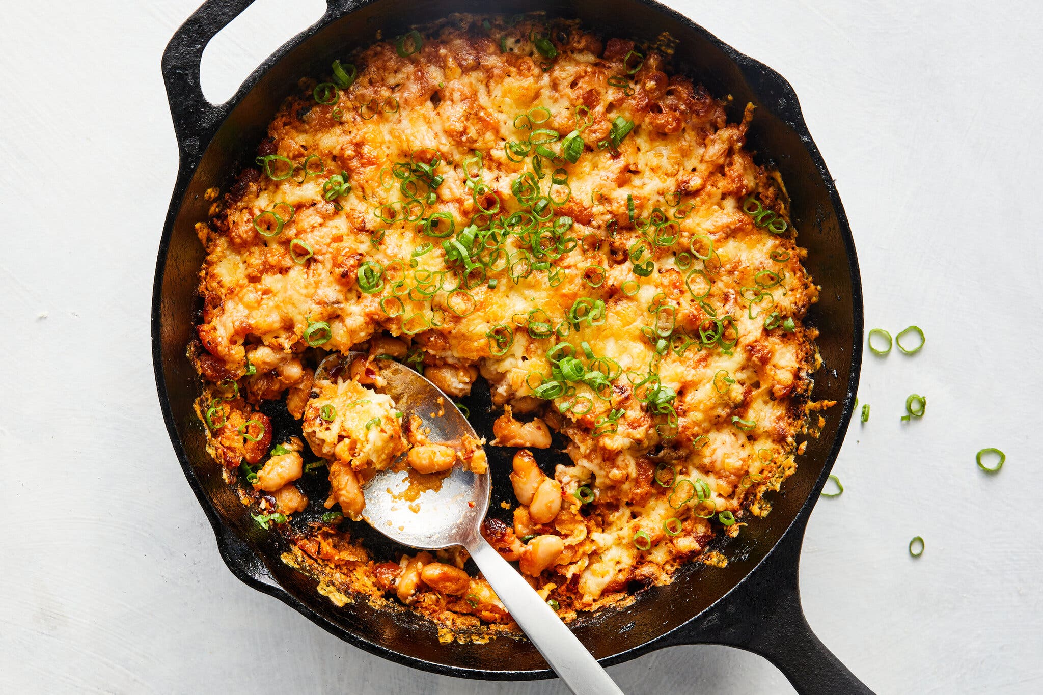 A cast-iron skillet holds cheesy beans finished with thinly sliced scallion greens.