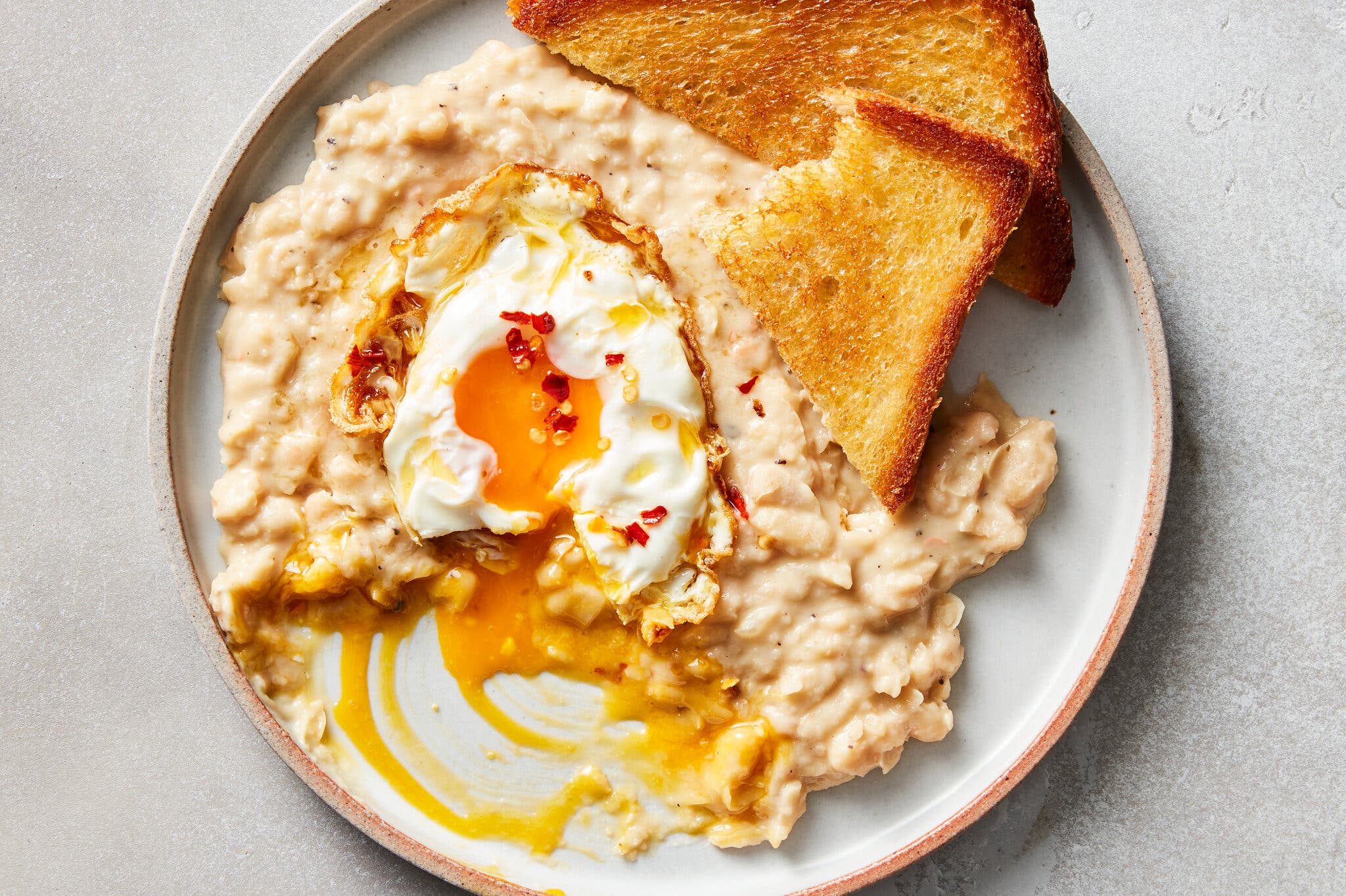 Refried white beans are topped with a jammy egg and paired with toast.