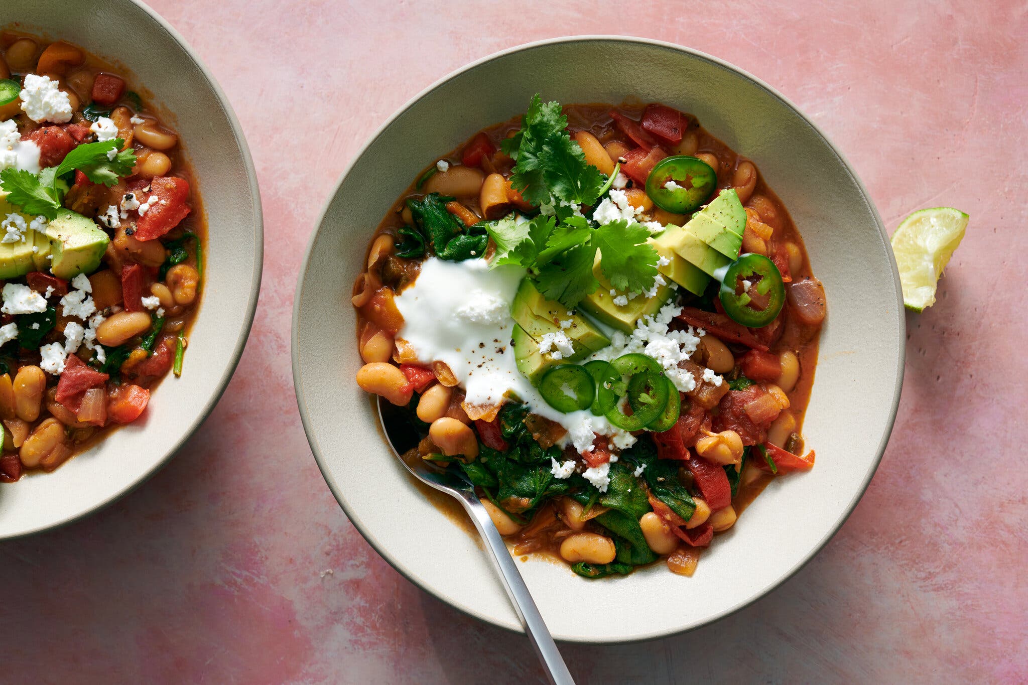 White beans in a red sauce are topped with avocado, herbs, cream and sliced jalapeños.