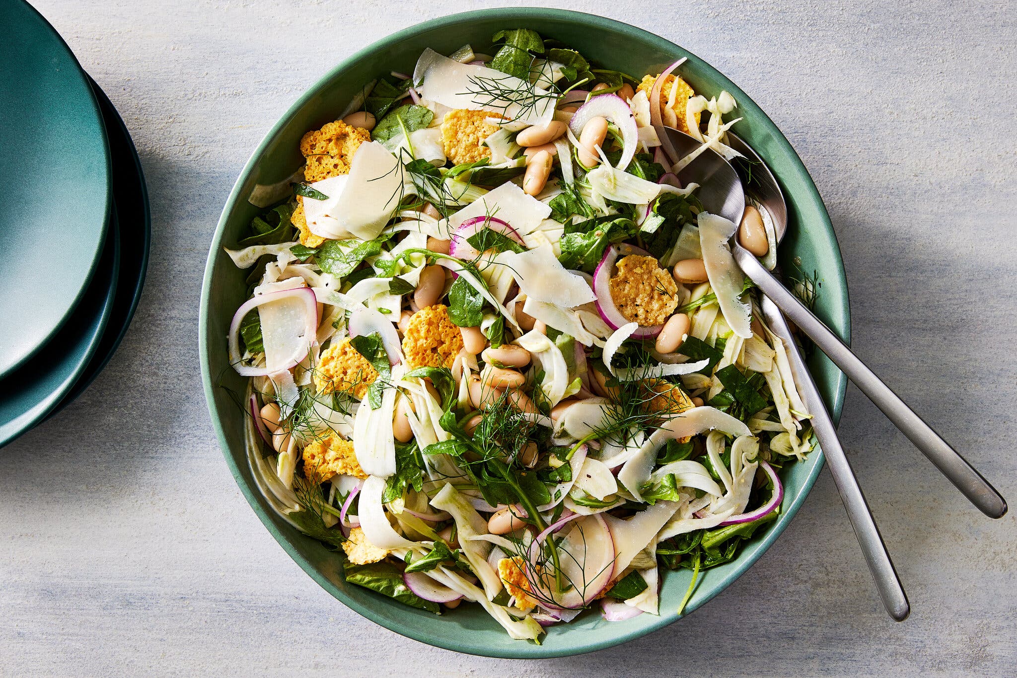 An aqua blue bowl holds a salad of herbed white beans topped with cheese and strips of red onion.