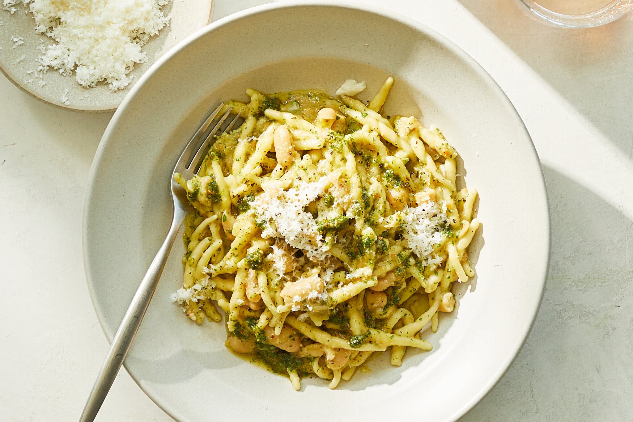 Creamy pasta with white beans is topped with cheese and pesto.