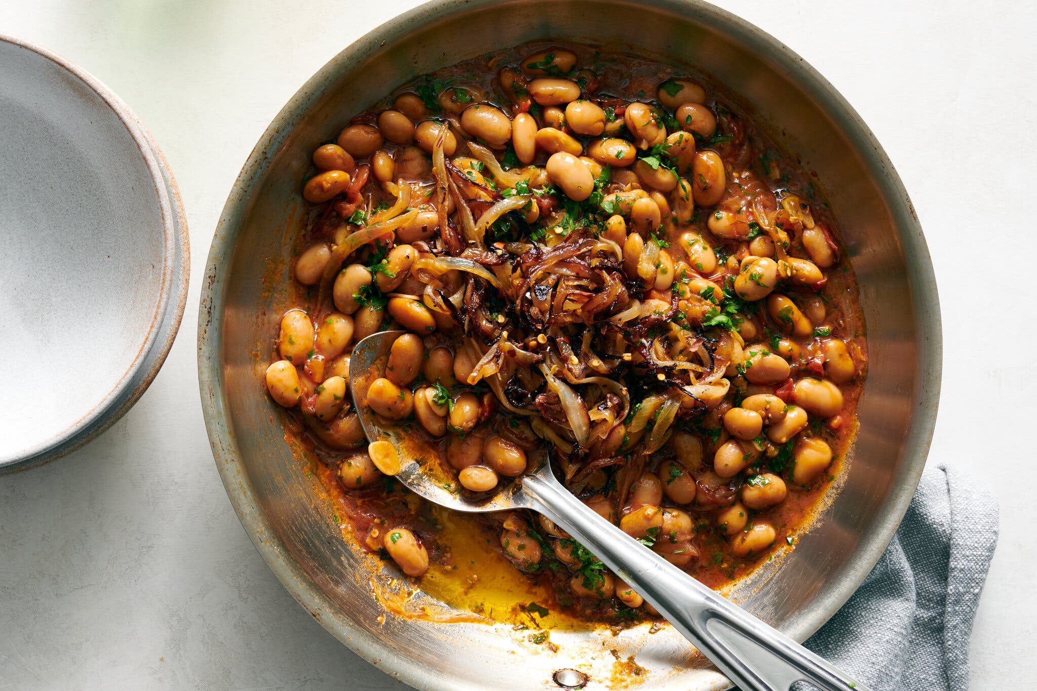 White beans in a dark red tomato sauce are topped with frizzled onions.