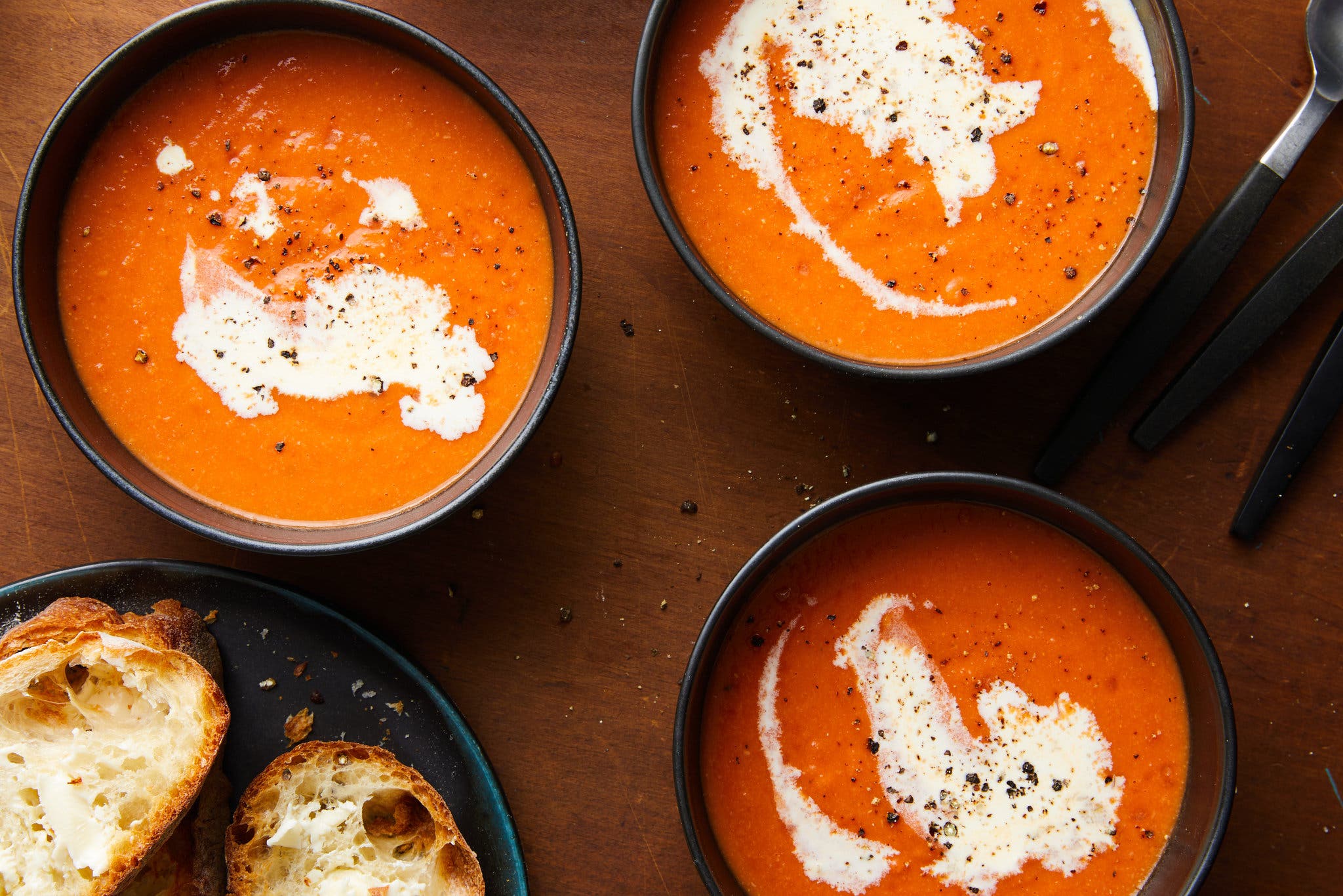 Three bowls of a tomato-red soup are finished with dollops of cream.