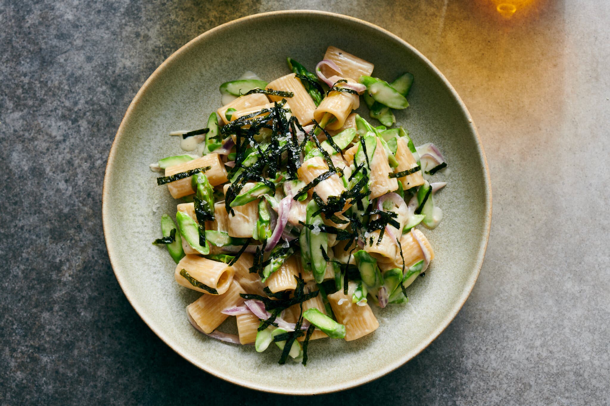 An overhead image of creamy short pasta topped with asparagus and slivered seaweed.