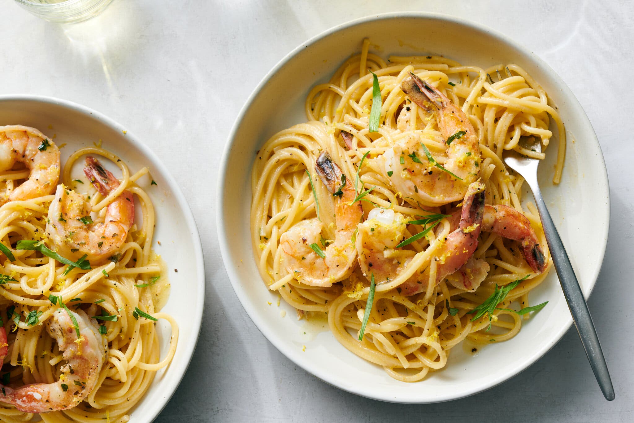 Two bowls of pasta topped with tail-on shrimp.