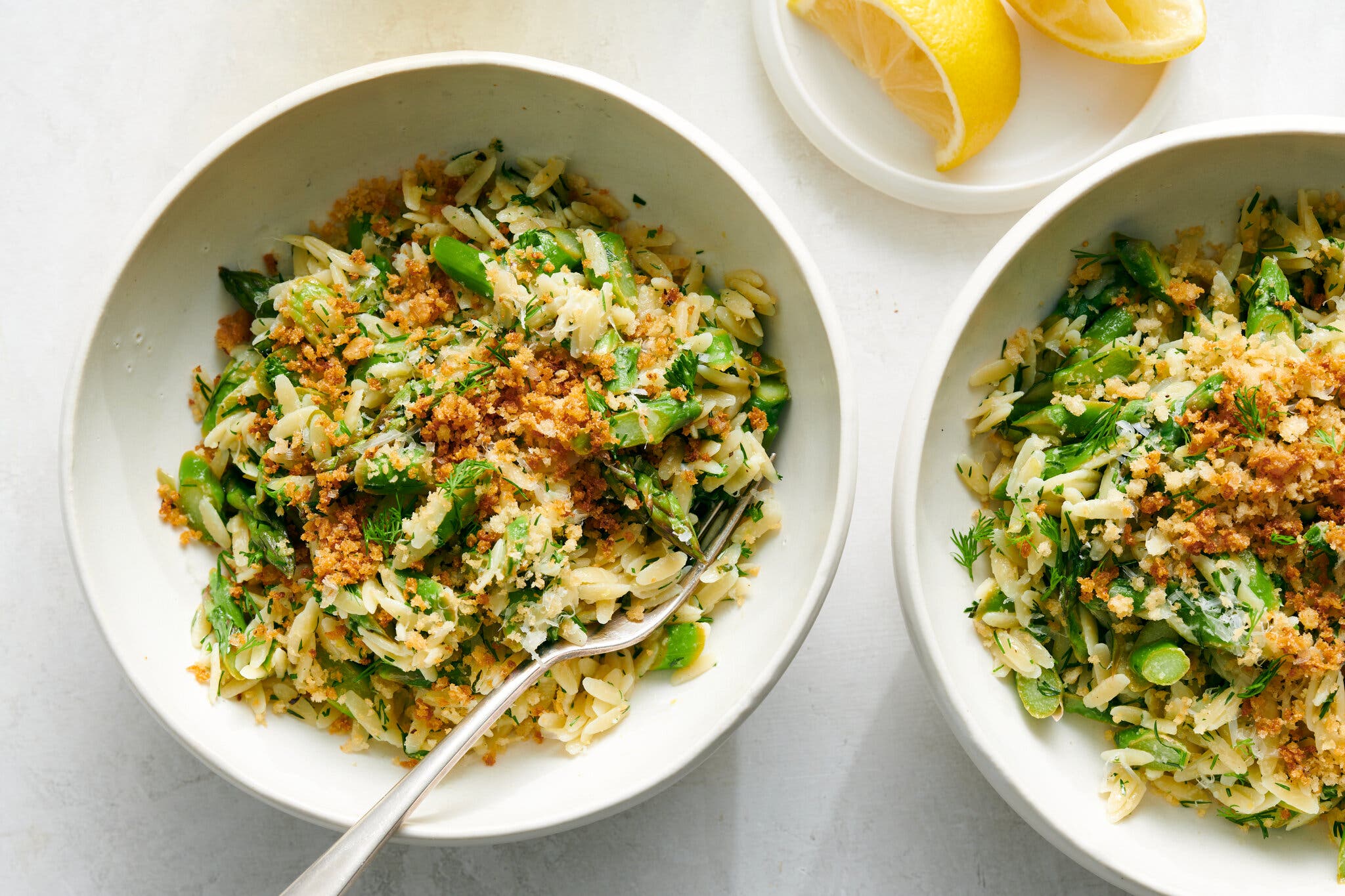 Orzo and asparagus sit in white bowls, topped with asparagus.