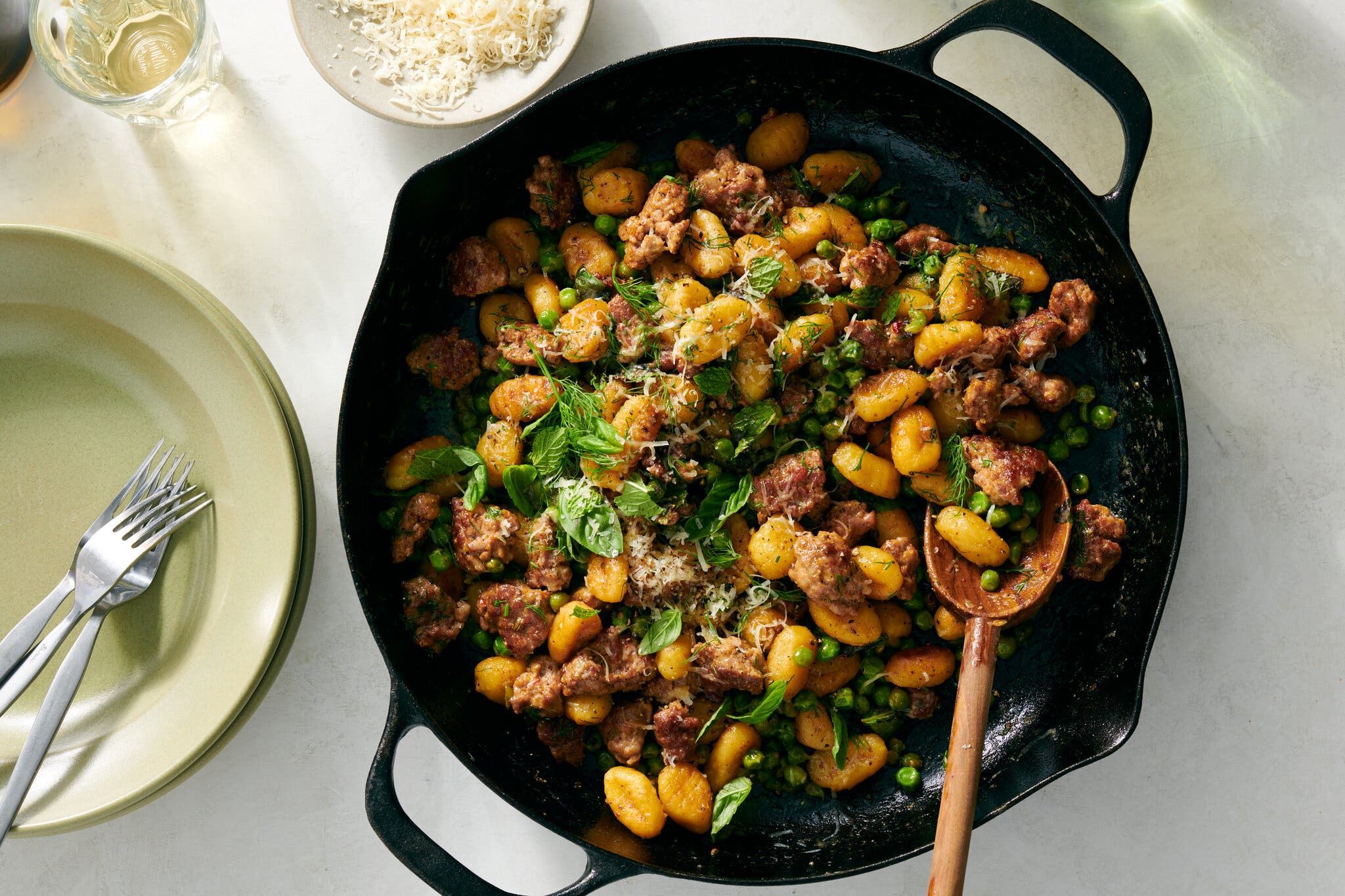 Gnocchi and pieces of sausage scattered with cheese and herbs sit in a cast-iron skillet.