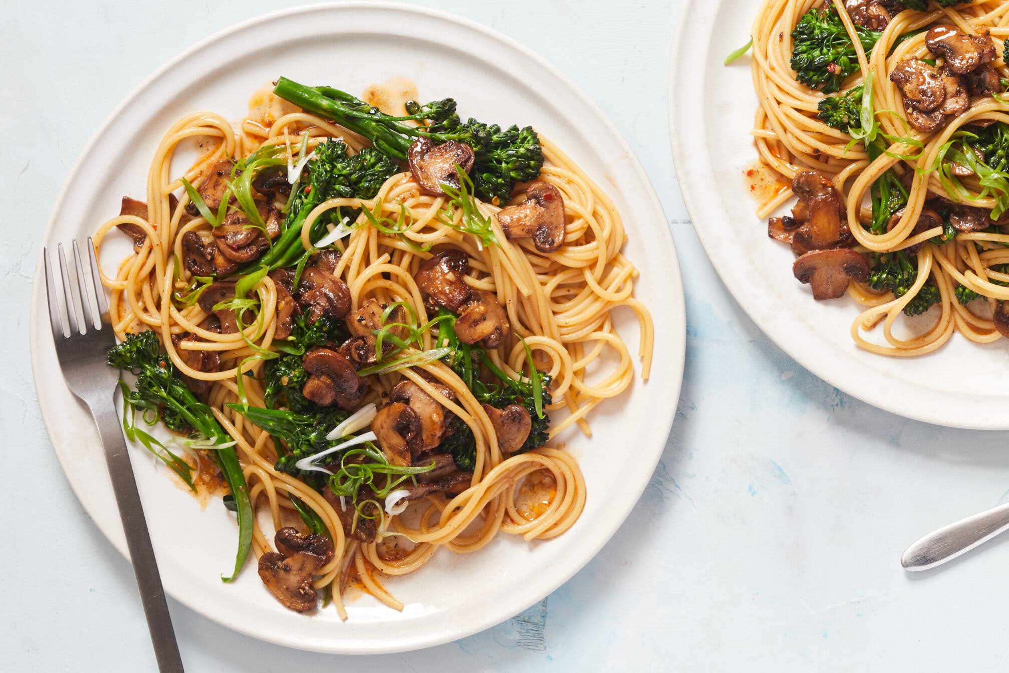 A plate topped with pasta, mushrooms and broccolini.