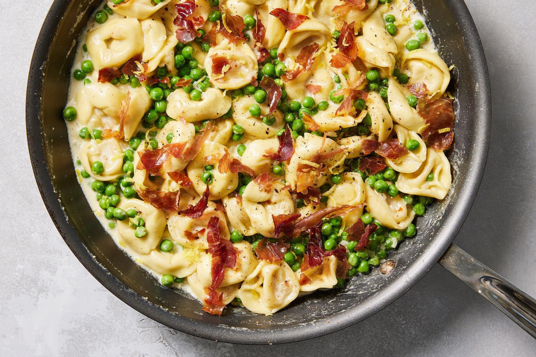 Tortellini topped with peas and prosciutto in a skillet.