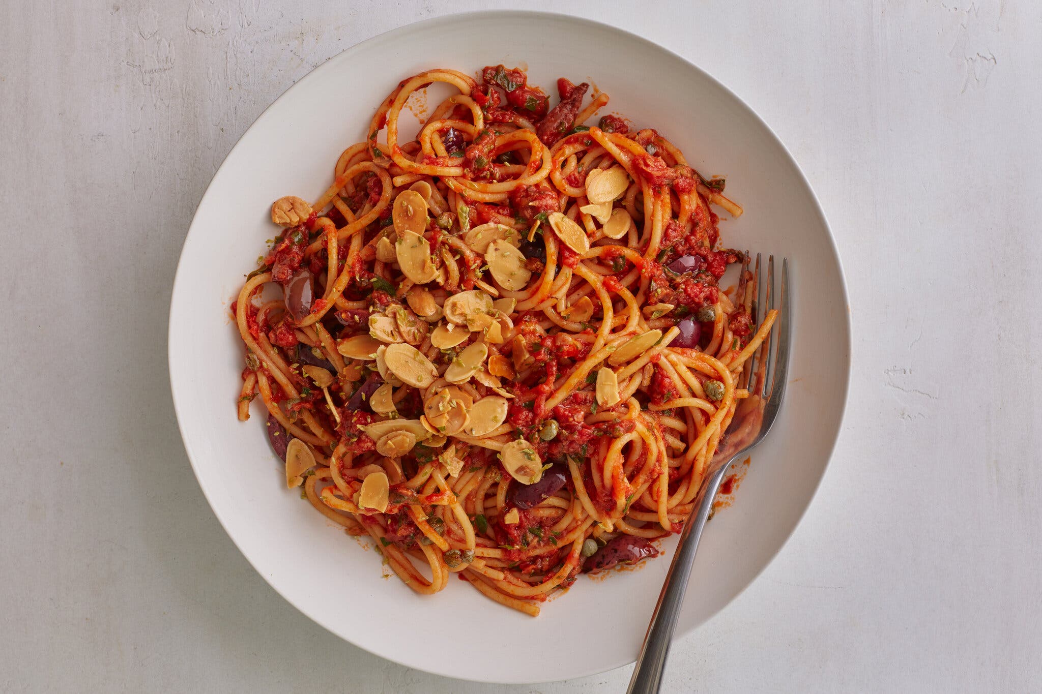 An overhead image of red-sauced pasta topped with slivered almonds.