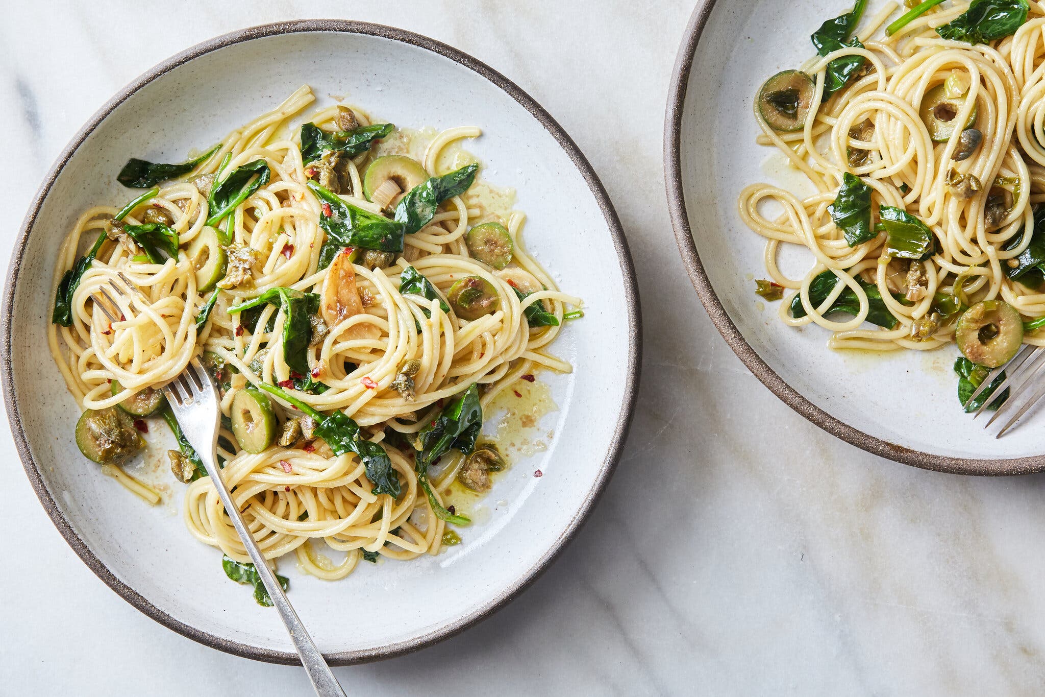 A plate topped with noodles tossed with olives and greens.