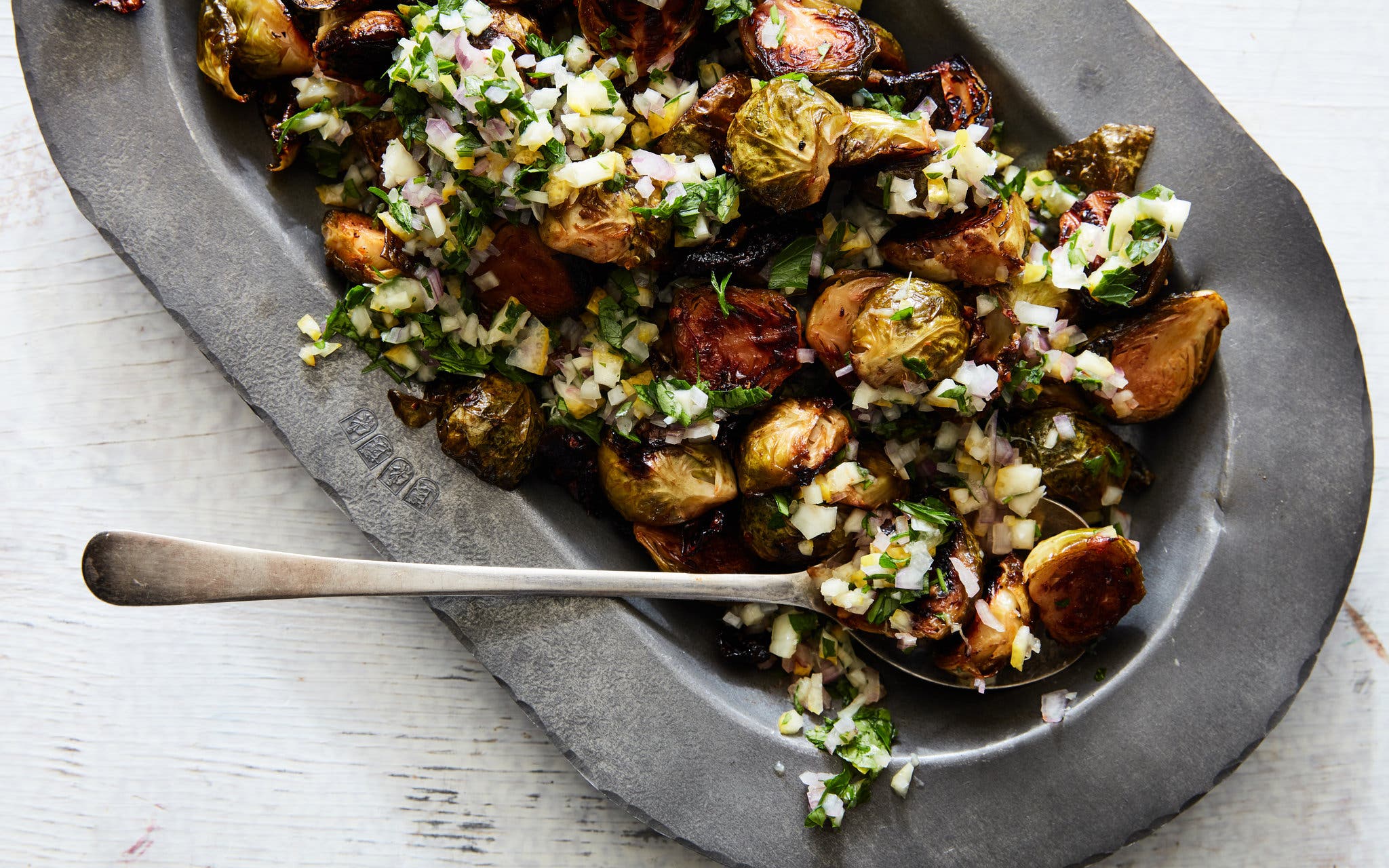 An overhead image of roasted brussels sprouts in a metal platter topped with a lemony relish.
