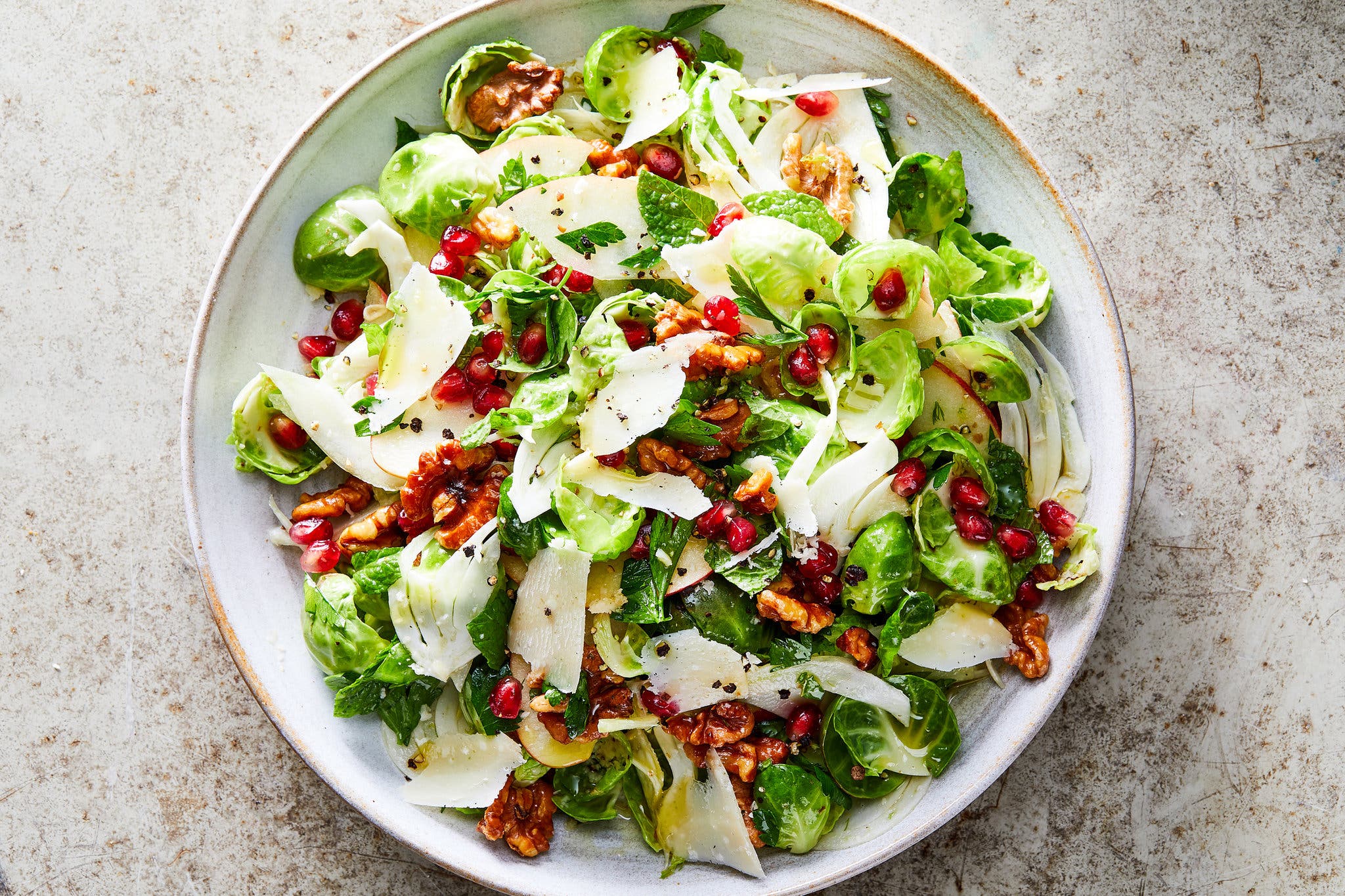 An overhead image of a brussels sprouts salad topped with pomegranates and walnuts.