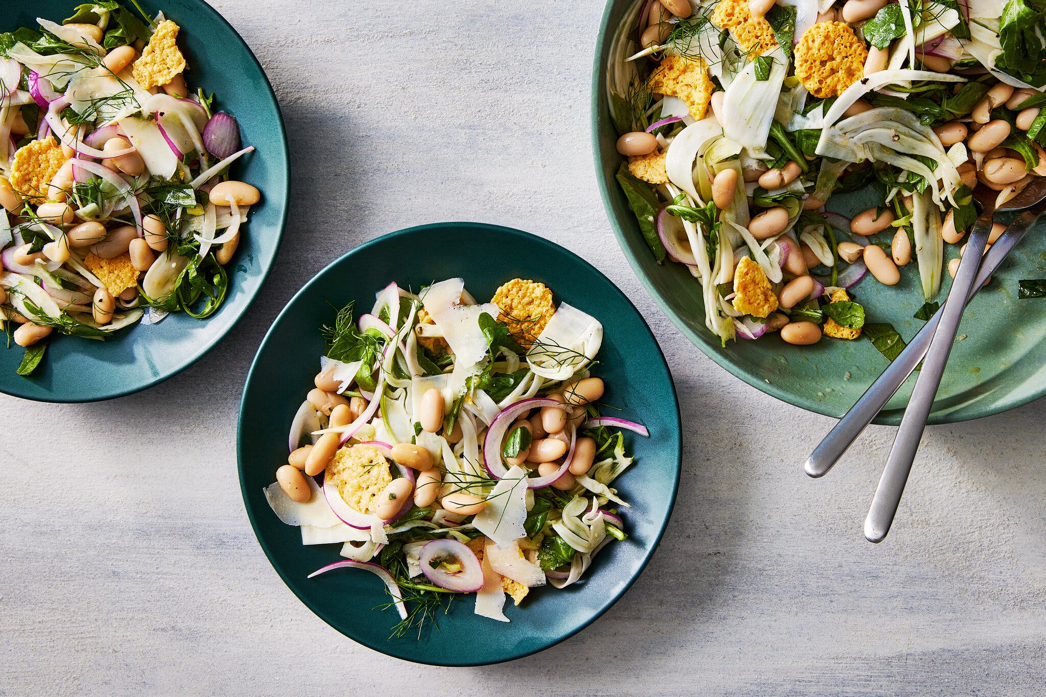 An overhead image of three bowls filled with white beans, crispy cheese and shaved fennel.