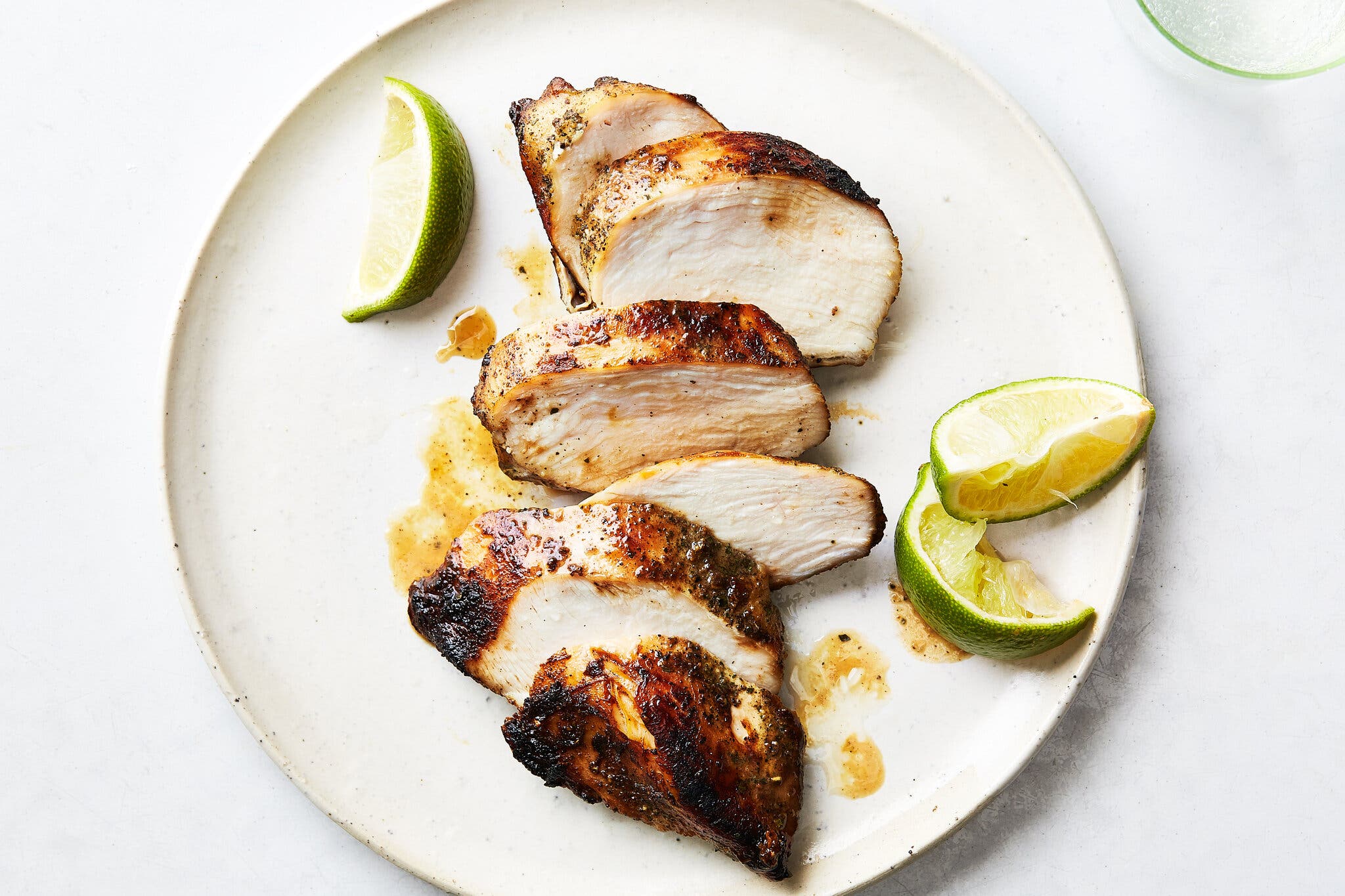 An overhead chicken of a sliced chicken breast on a white plate, next to lime wedges.