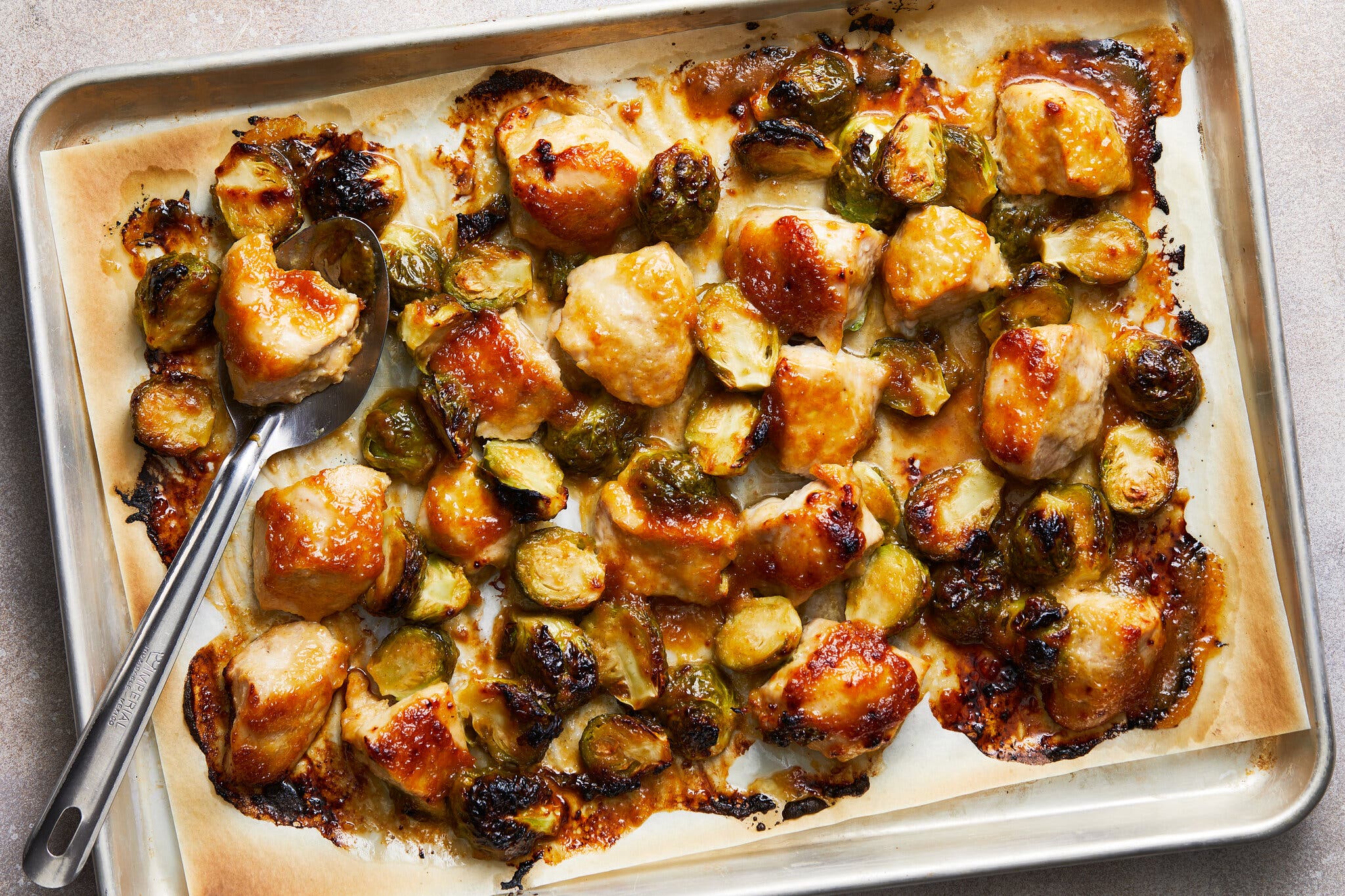 An overhead image of chicken breast chunks and halved brussels sprouts on a sheet pan.