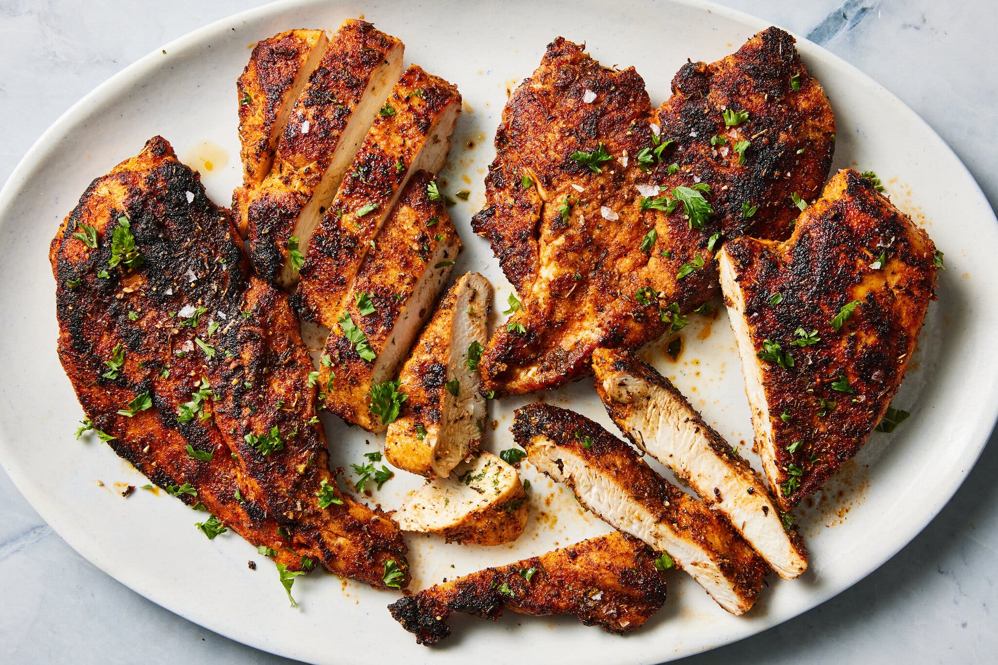 An overhead image of chicken breasts coated in a dark spice rub on a white platter.