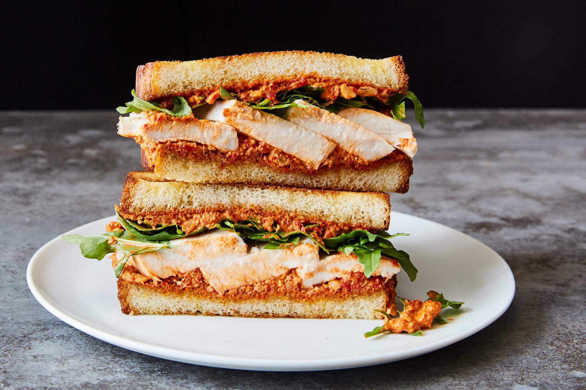 A side image of a halved chicken sandwich filled with muhammara.