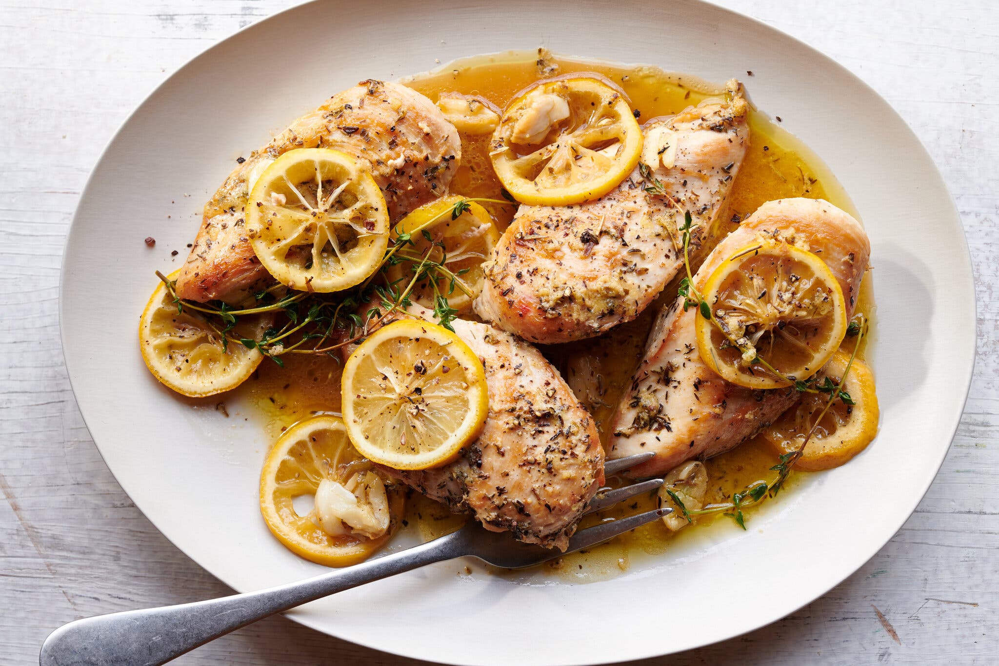An overhead image of chicken breasts on a platter topped with lemon wheels.