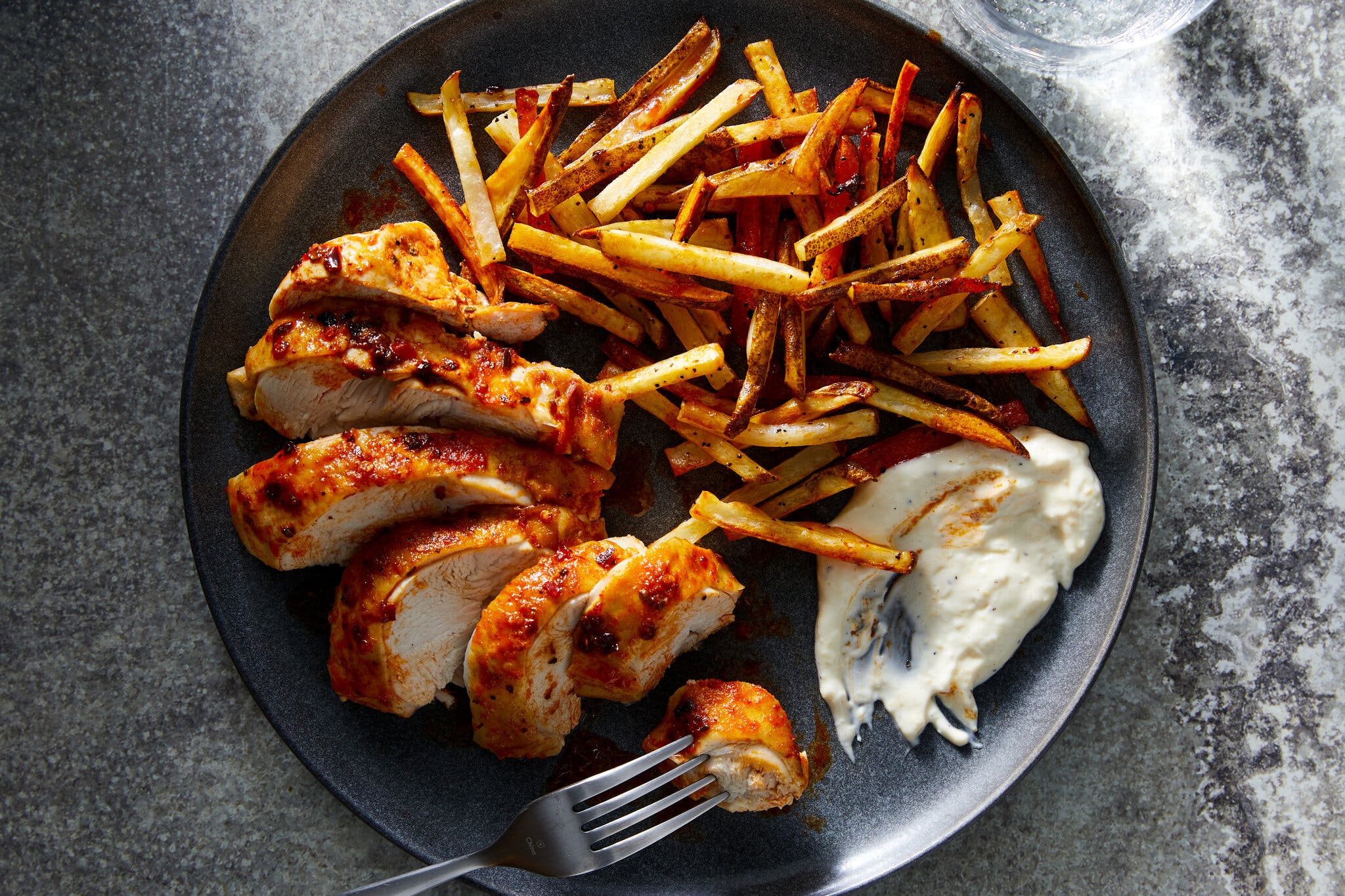An overhead image of a sliced chicken breast on a plate next to fries and a dipping sauce.