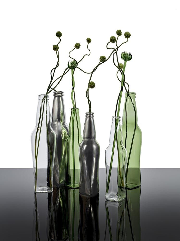 Van Assche’s modern take includes glass and metallic bottle-shaped vases, blending minimalism with sculptural elegance.