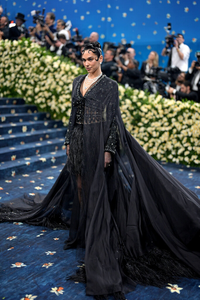 Dua Lipa is wearing a black gown with a sheer cape.
