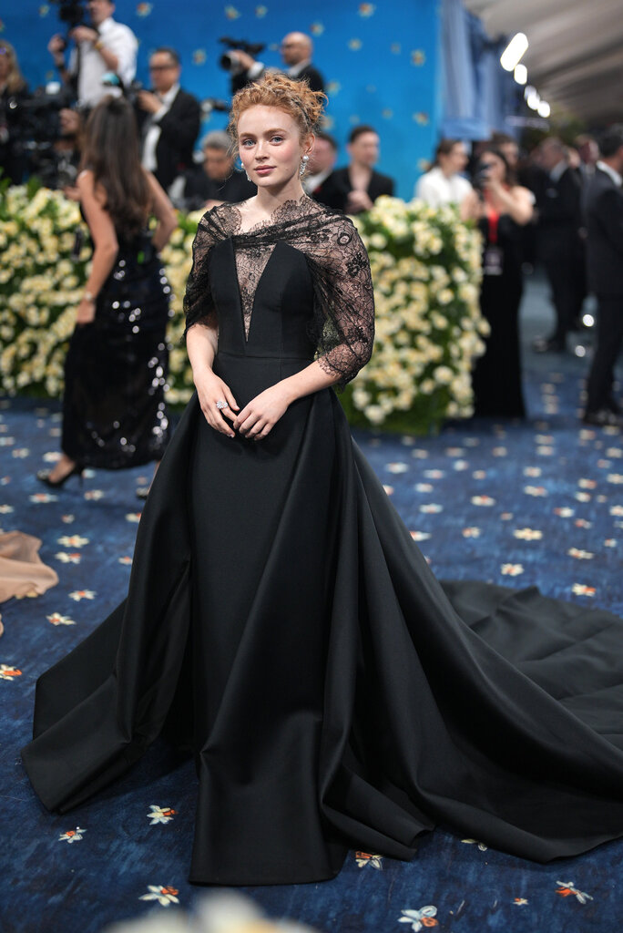 Sadie Sink wearing a black floor-length gown with lace detailing along the neckline and shoulders.