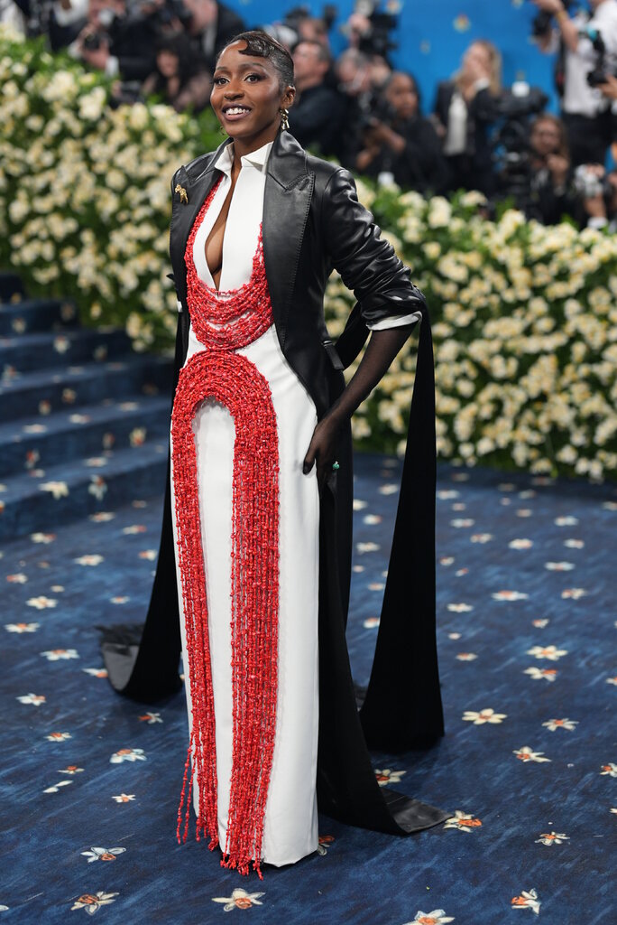 Ayo Edebiri wearing a long white dress with dramatic red beads and a long black leather coat.