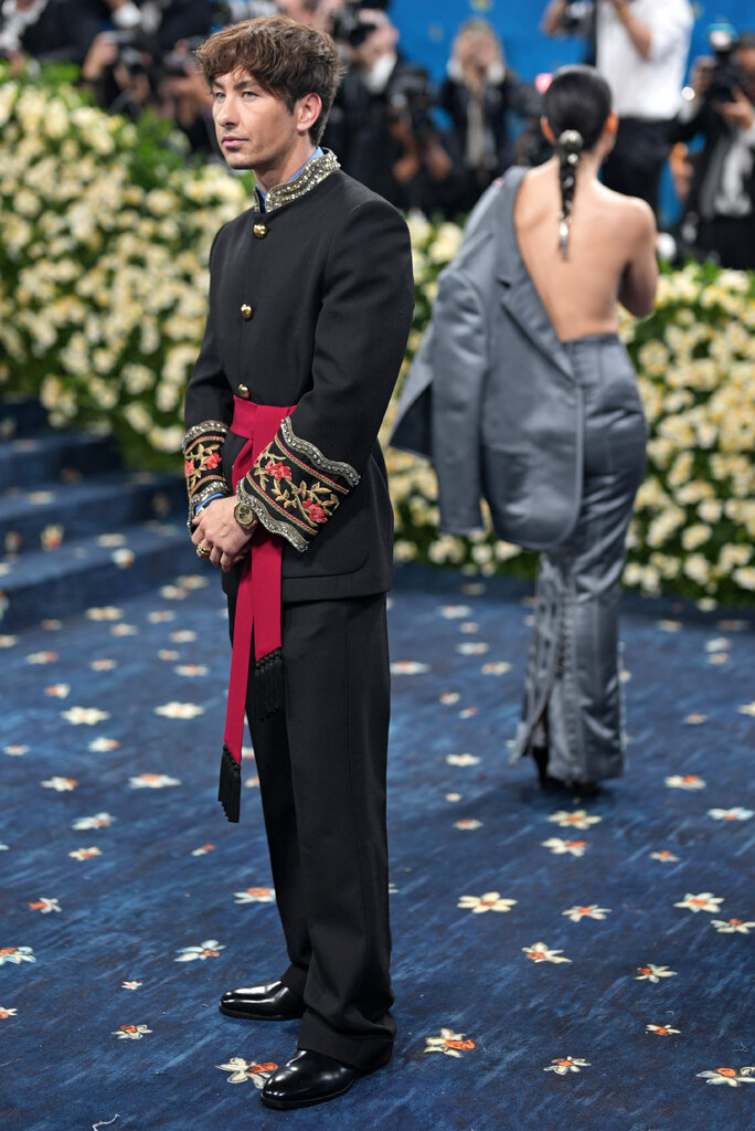 Barry Keoghan wearing a black suit with embroidered details at the cuffs and a red sash belt.