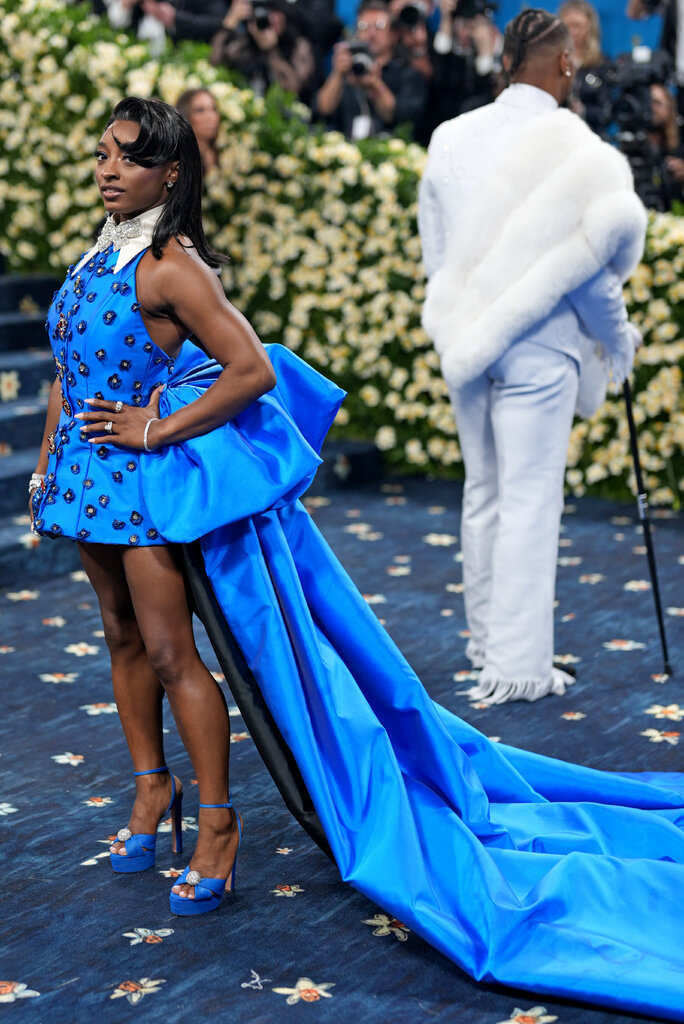 Simone Biles is wearing a blue dress with a long train.