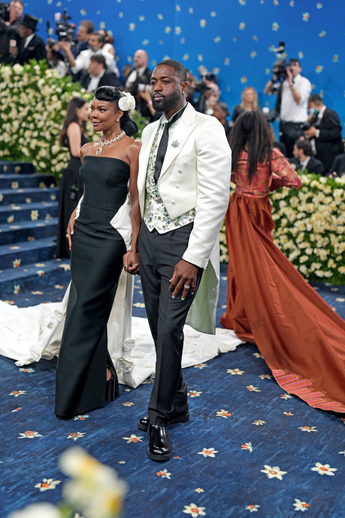 Dwyane Wade, wearing a white suit jacket and black pants, and Gabrielle Union, wearing a long, black sleeveless dress.