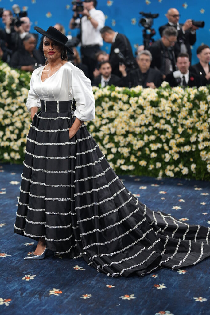 Ava DuVernay is wearing a striped skirt, white bodice and black hat with a veil.