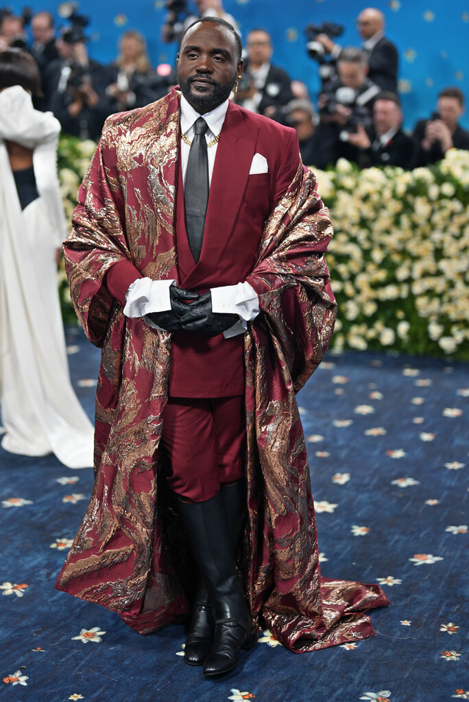 Brian Tyree Henry wearing a red satin suit, gold robe and knee-high boots.