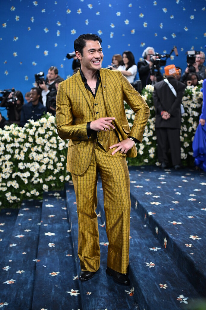 Henry Golding is wearing a gold patterned suit.