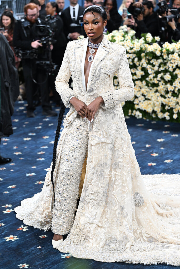 Coco Jones is wearing a jeweled white suit with a long train.