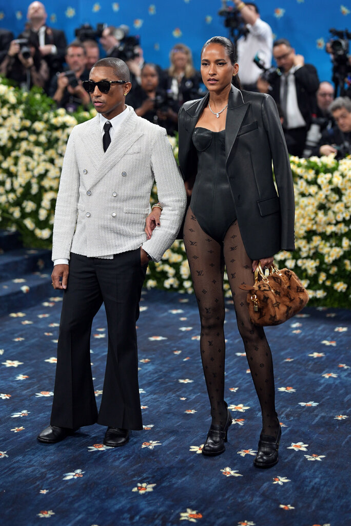 Pharrell Williams is wearing a suit with a gray blazer and Helen Lasichanh is wearing a black bodysuit.