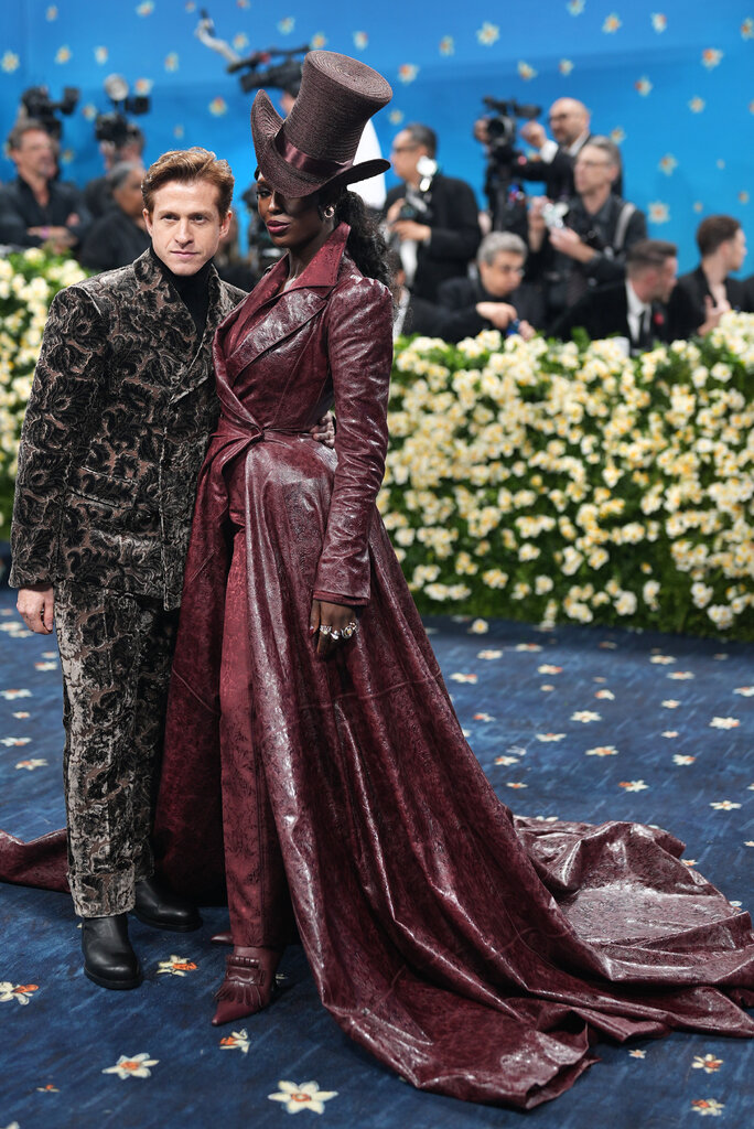 Jodie Turner-Smith is wearing a maroon suit with a long matching leather jacket and top hat. Daniel Lee is wearing a brown velvety suit.