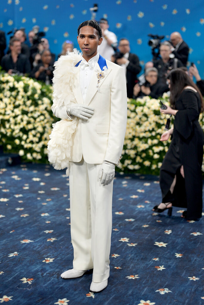Tyler Mitchell wearing a cream suit with blue detailing at the collar, a feathered shoulder and cream gloves.