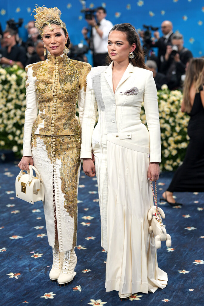 Wendi Murdoch, wearing a form-fitting jacket with gold embroidery, and Grace Murdoch, wearing a white, patchwork dress.