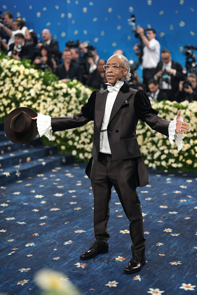 Al Sharpton wearing a dark-brown suit with velvet shoulders, pleated white sleeves and a white bowtie.