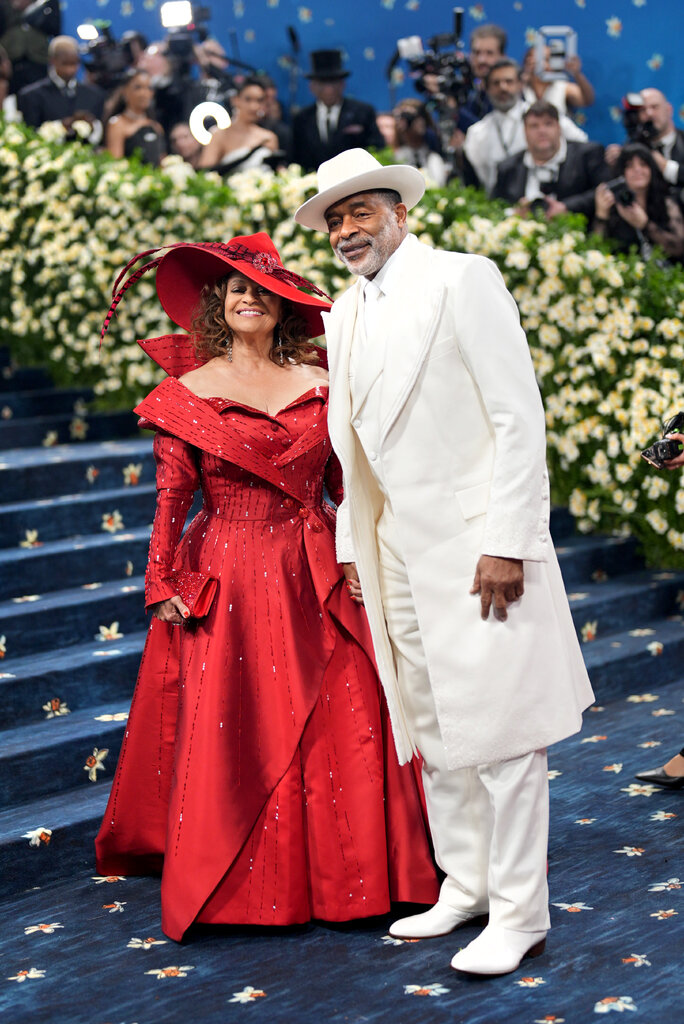 Debbie Allen is wearing a red gown with matching hat and Norm Nixon is wearing a white suit with matching hat.