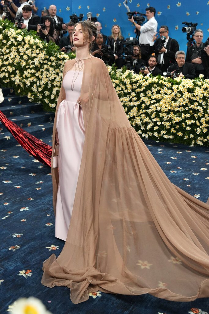 Maya Hawke wearing a blush pink gown with a sheer, floor-length beige cape tied at the neck.