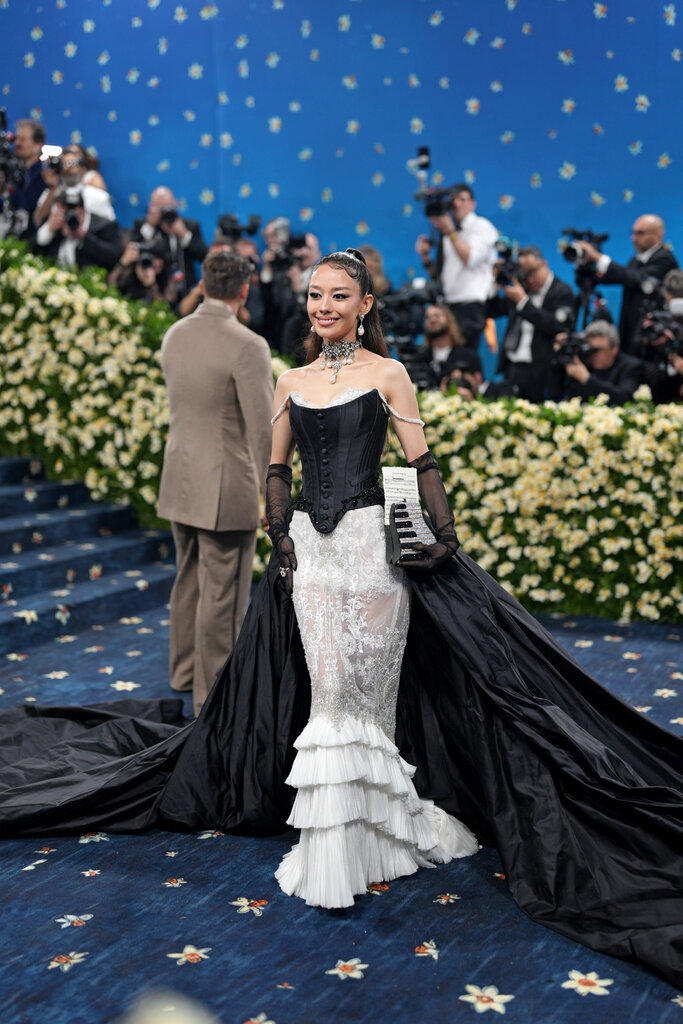 Gina Alice Redlinger, wearing a black and white mermaid gown with ruffles and an exaggerated train, poses holding a keyboard-shaped handbag.