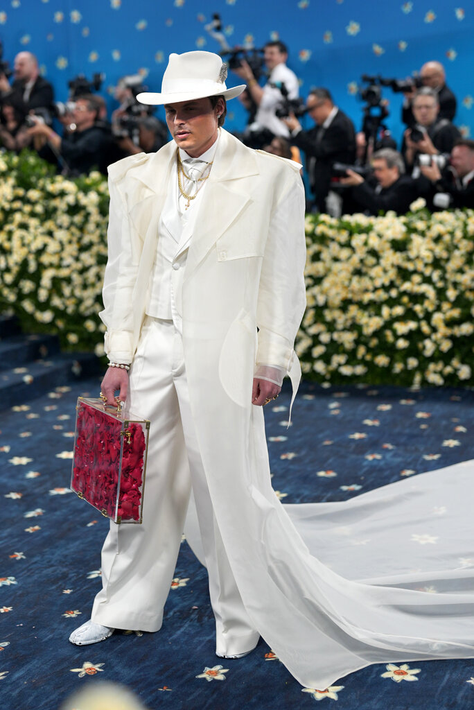 Gustav Magnar Witzoe, wearing a cream suit, poses holding a clear briefcase with red roses inside.