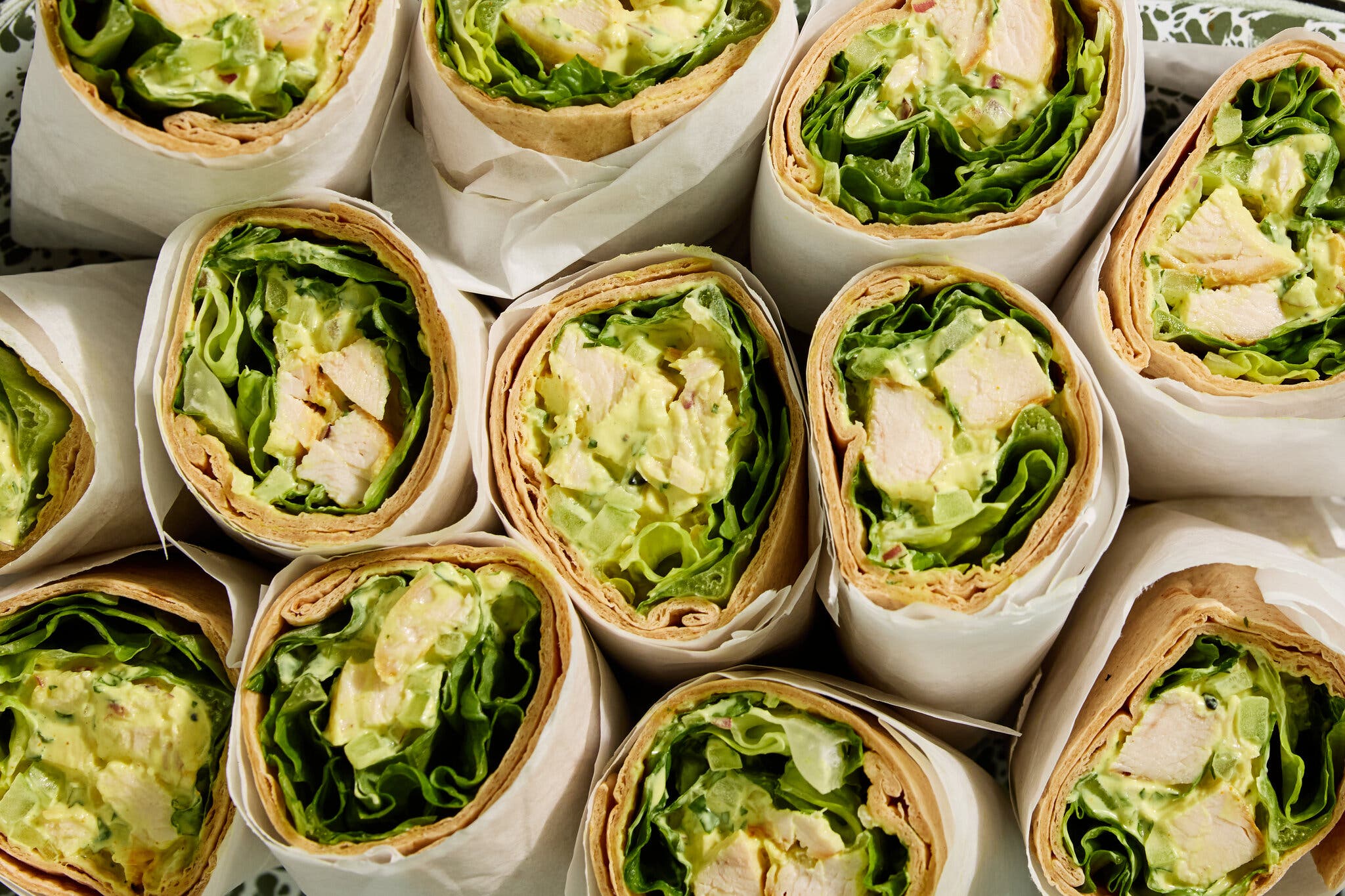 An overhead image shows cross sections of chicken salad wraps that have been rolled in parchment paper.