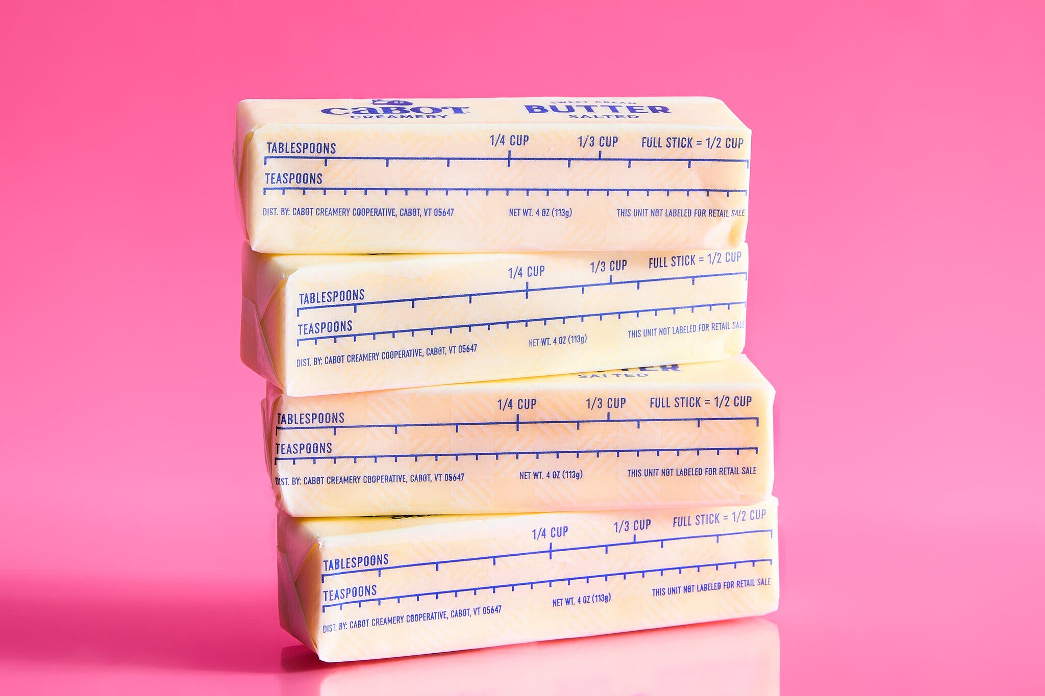 Four sticks of butter stacked against a pink background.