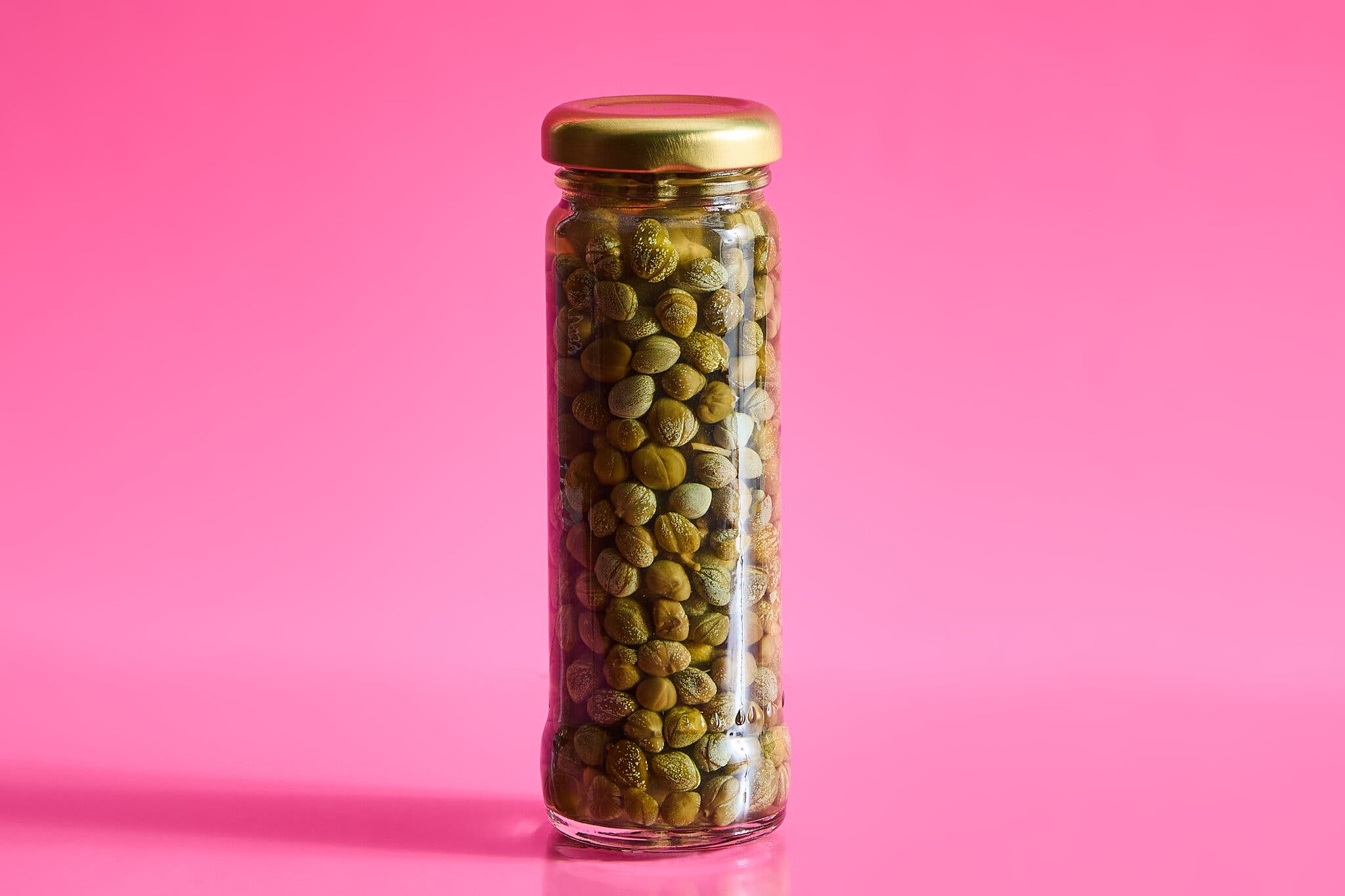 A jar of capers against a hot pink background.