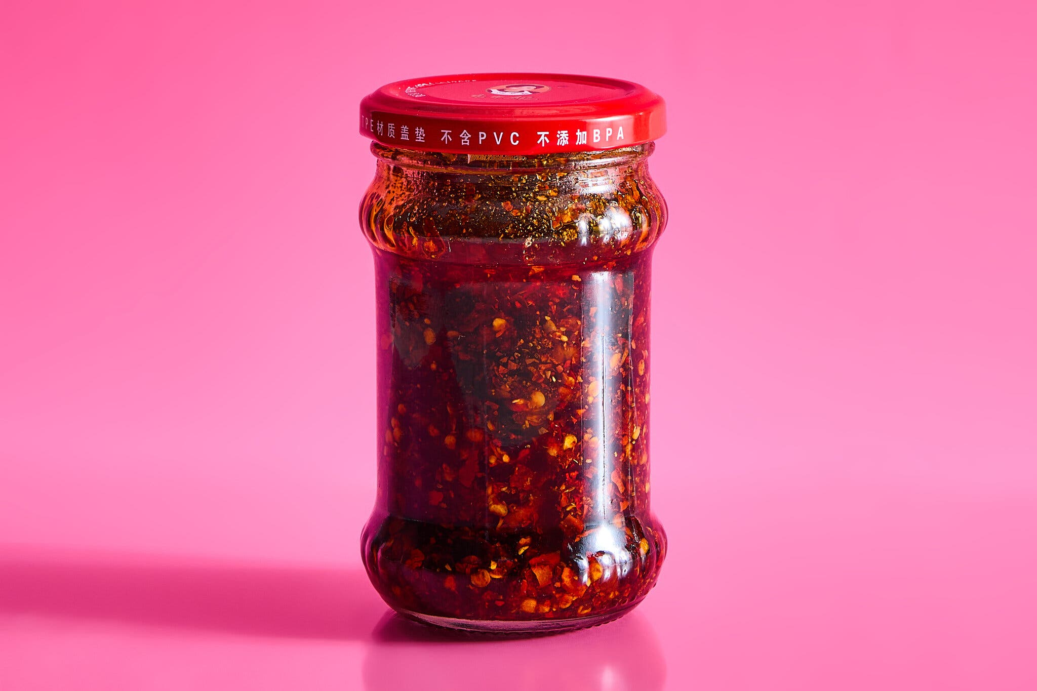 An unlabeled jar of chile crisp against a hot pink background.